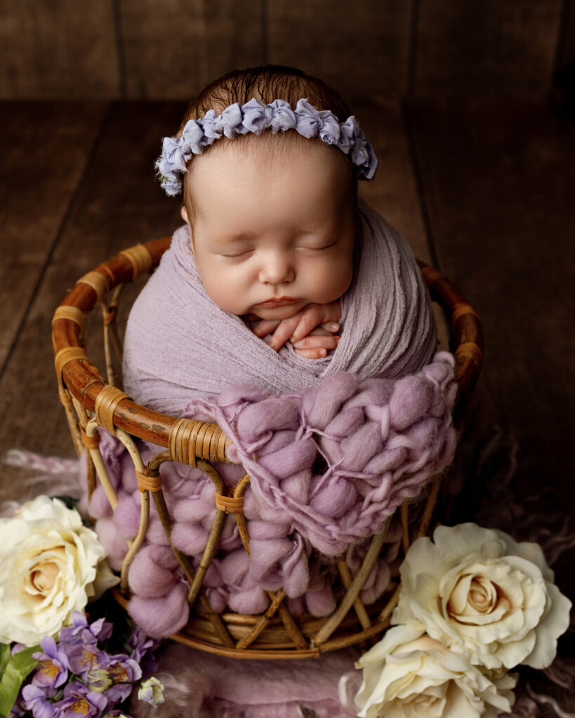 Peaceful newborn portrait in a lavender wrap and ribbon headband by a newborn photographer in the Inland Empire.