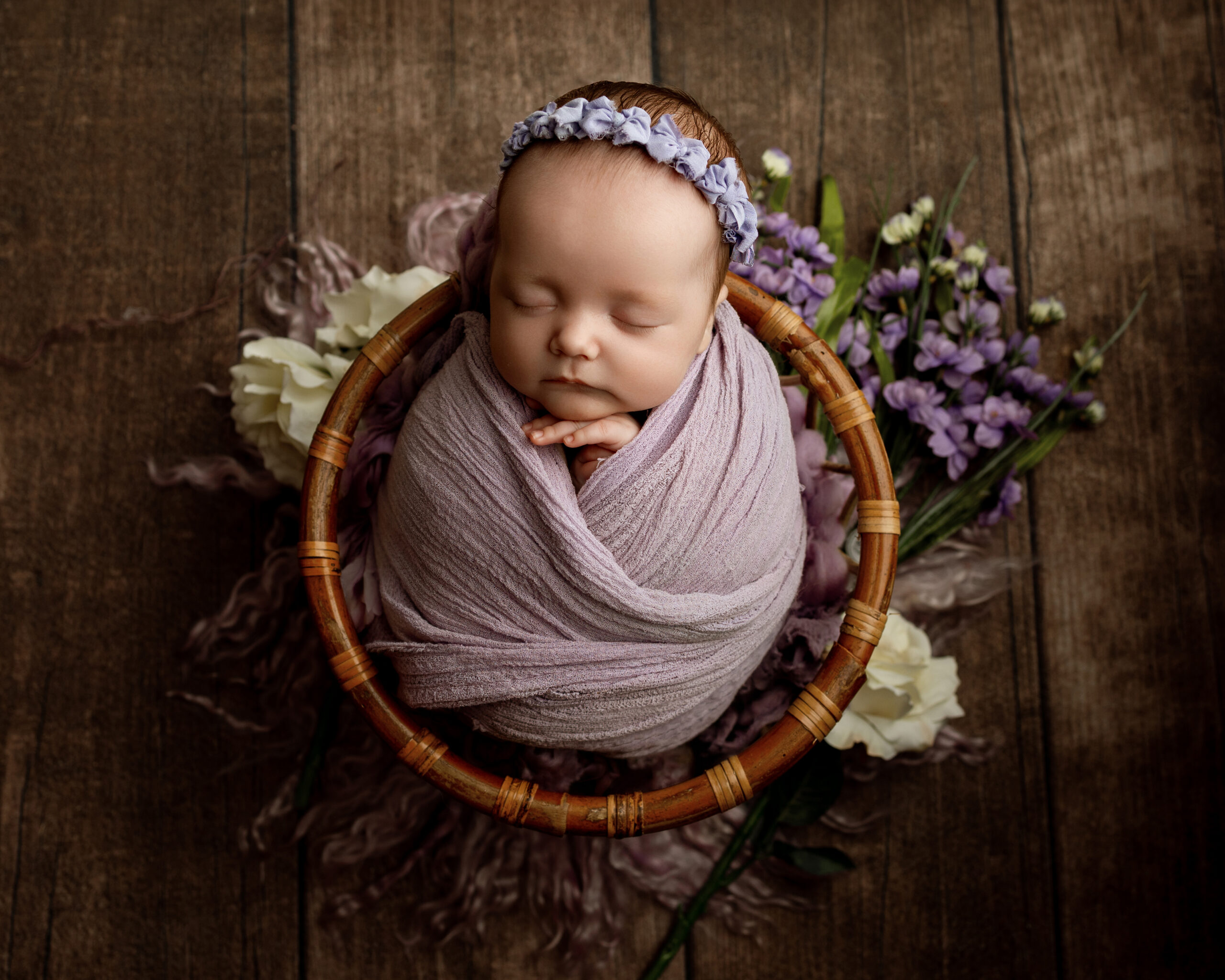 2 month old baby milestones illustrated with a peaceful newborn wrapped in a lavender swaddle, sleeping in a rustic basket surrounded by purple flowers.