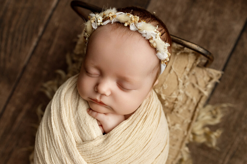 Studio newborn portrait of a sleeping baby wrapped in a cream swaddle in a vintage bed, highlighting 2 month old baby milestones and precious early memories.