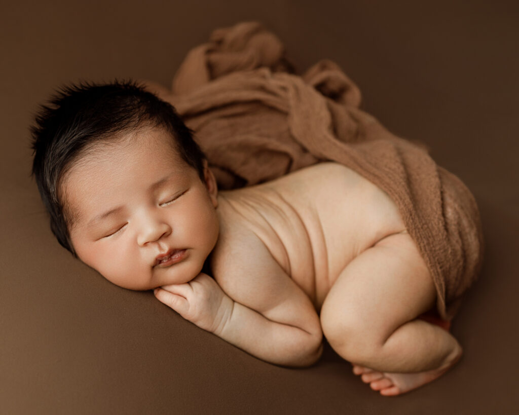 6 week old baby in newborn session in Yucaipa newborn studio, curled up in a cozy pose with a neutral brown wrap.