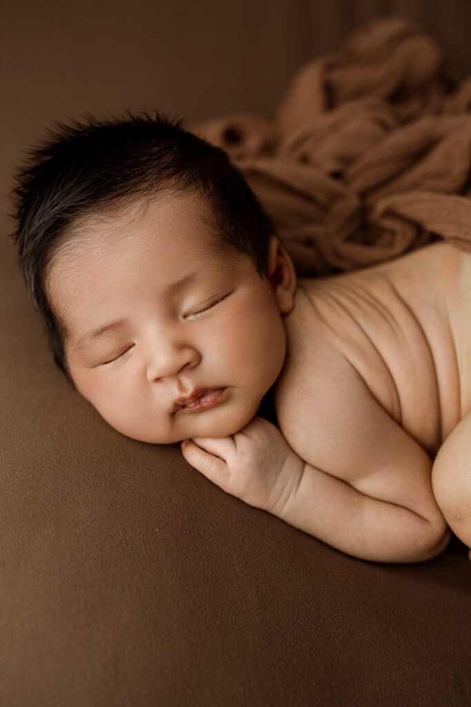 Close-up portrait of a 6 week old baby in newborn session in Yucaipa newborn studio, sleeping peacefully on a soft brown blanket.