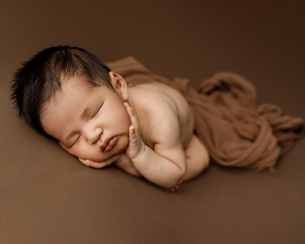 6 week old baby in newborn session in Yucaipa newborn studio, peacefully sleeping with head resting on folded hands.