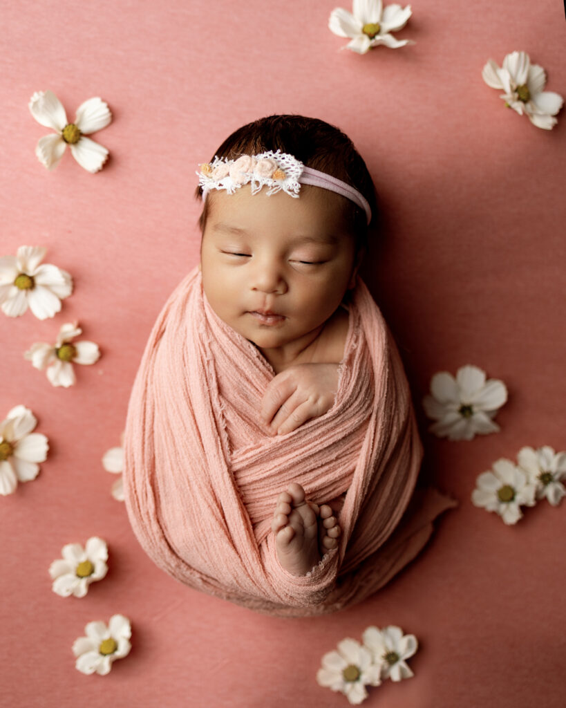 Peaceful newborn sleeping in a pink wrap on a floral backdrop for a guide about baby growth spurts.