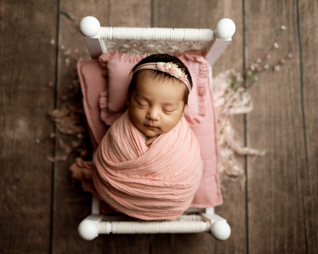 Newborn girl sleeping in a pink swaddle on a miniature bed, highlighting growth spurts and early baby development.