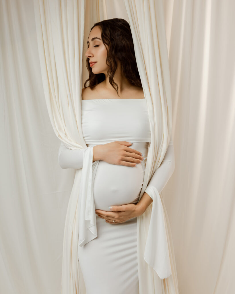 Side profile of a mother in her third trimester gently holding her baby bump in a timeless maternity portrait.